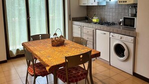 A modern kitchen with a dining table, chairs, a washing machine, and a microwave. - Appartamento San Massimo (Verona)