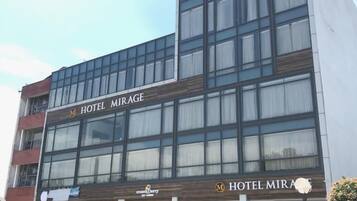 Um hotel com vários andares chamado "Hotel Mirage", com design arquitetônico moderno, grandes janelas e um logotipo marcante.