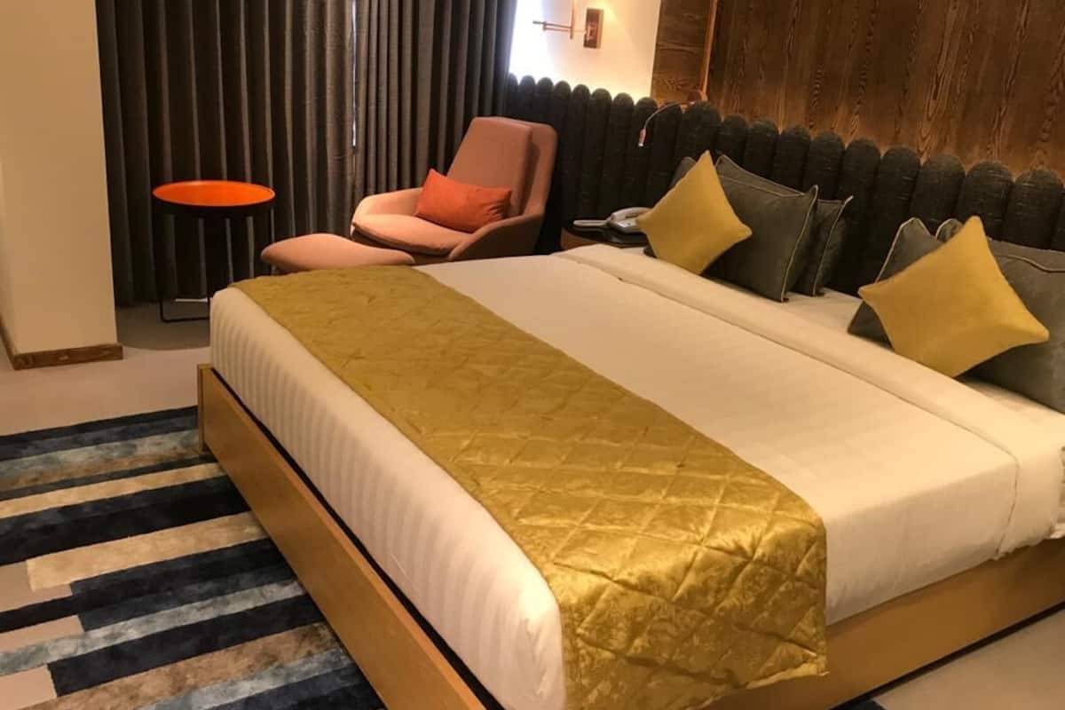 A hotel room with a large bed, a small round table, a chair, and a wall-mounted lamp.