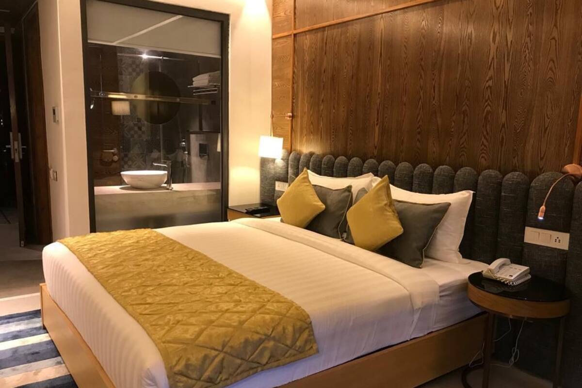 A neatly made bed with a yellow throw, a wooden headboard, and a bedside table with a phone.
