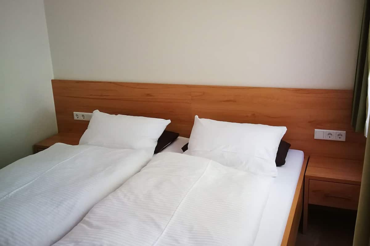 A double bed with white linens, a wooden headboard, and a nightstand with a power outlet.