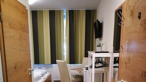 A compact room with a bed, a desk, a chair, and a small shelf. - HopfenErlebnisHof (Altmannstein)
