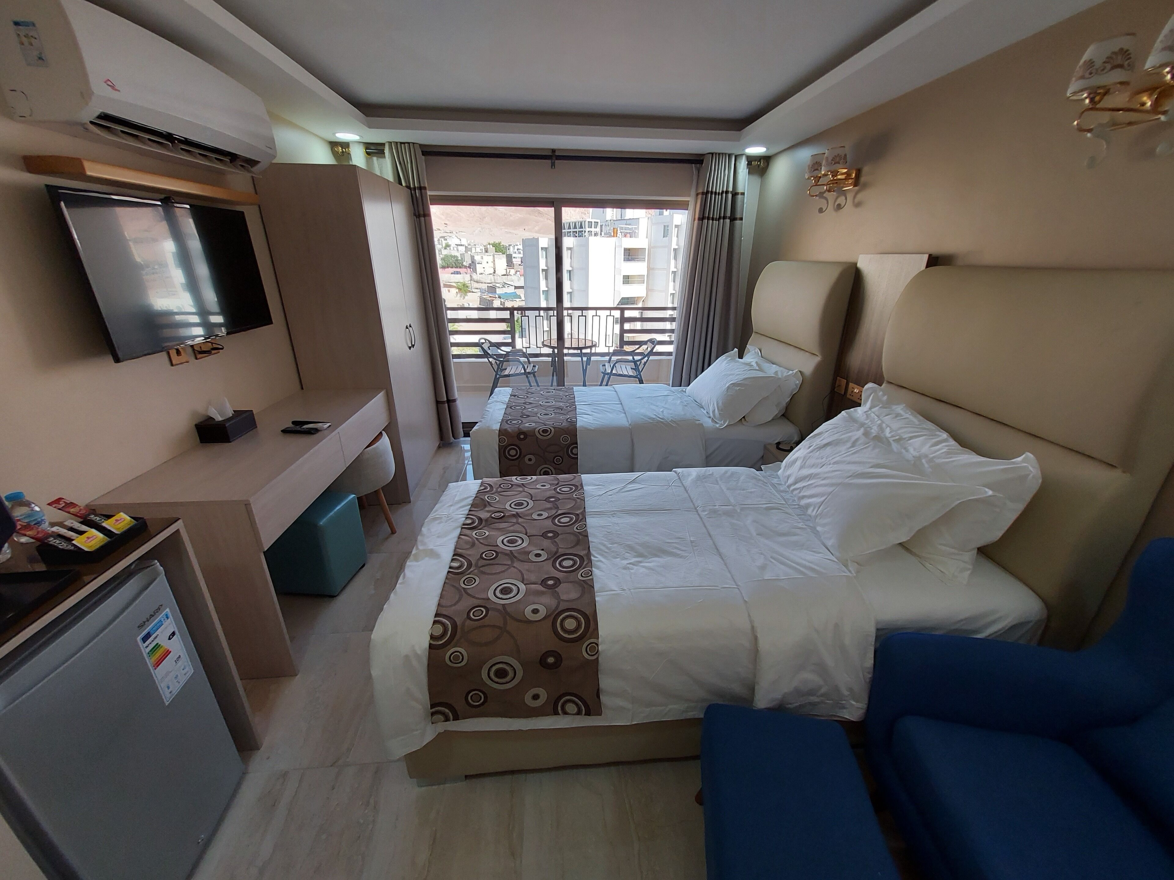 A hotel room with two beds, a TV, a desk, and a mini-fridge.