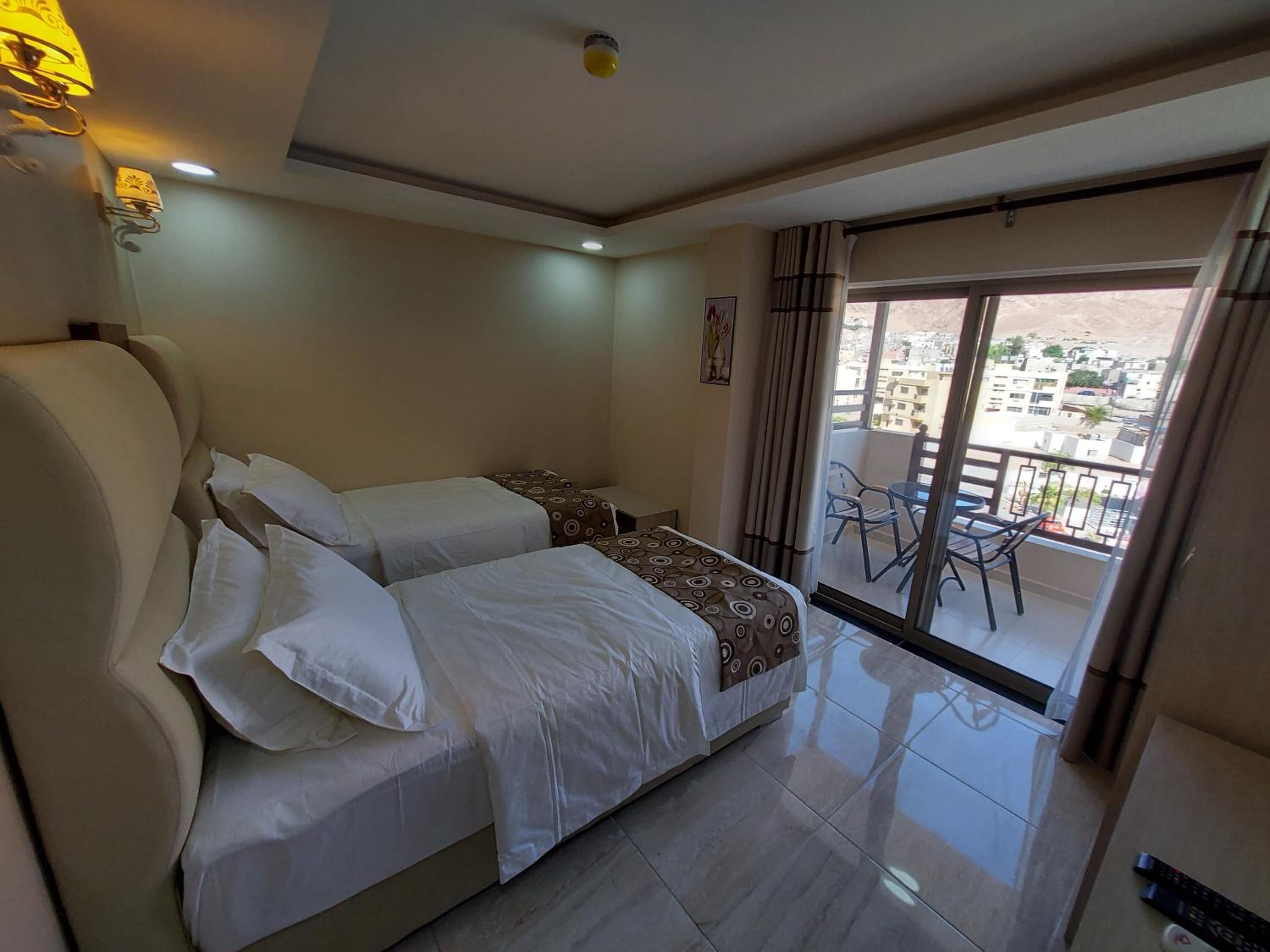 A hotel room with two beds, a balcony with chairs, and a view of the city.