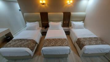 A hotel room with three single beds, each with a patterned bedspread and white pillows. There are two wall-mounted light fixtures above the beds.