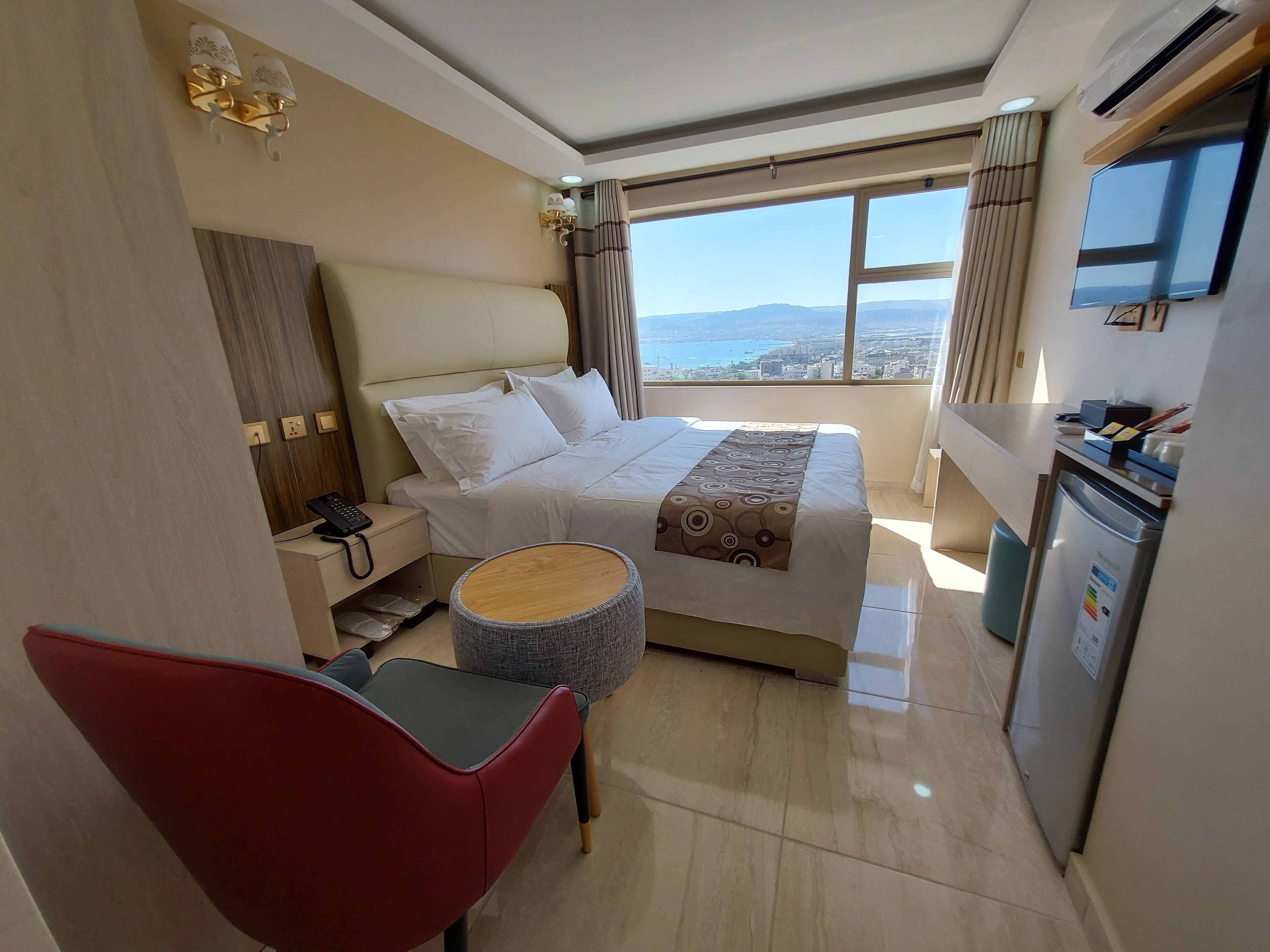 A hotel room with a bed, a desk, a chair, a TV, and a view of the city.