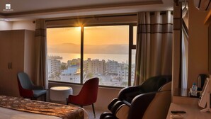 A hotel room with a large window, a bed, a desk, a chair, and a massage chair. - Jordan Seasons Hotel (Aqaba)