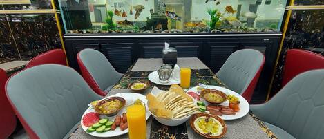 A dining area with a marble table, red and grey chairs, a fish tank, and a variety of food items.