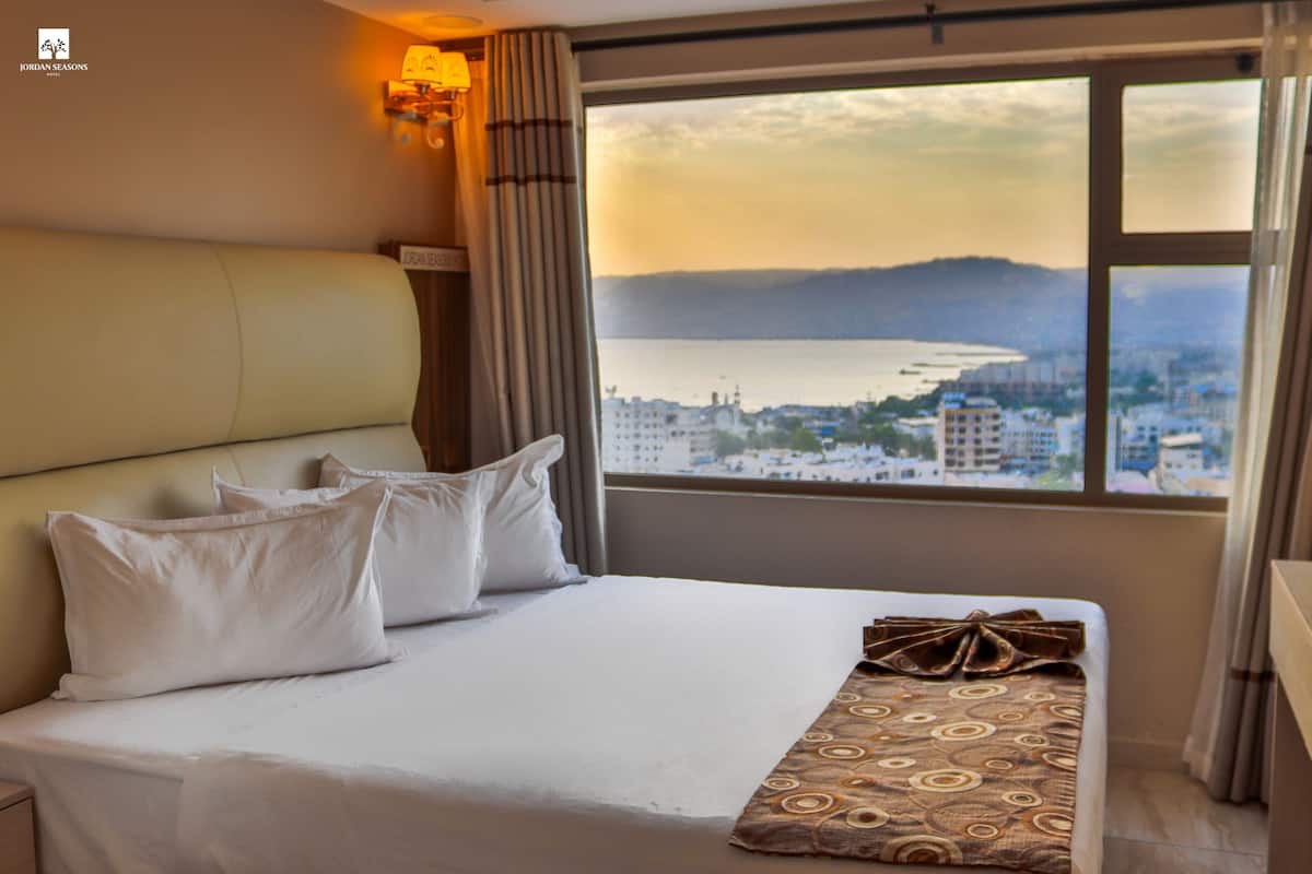 A hotel room with a bed, a view of a cityscape, and a window with curtains.