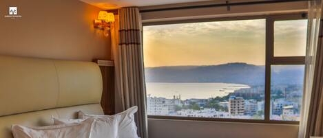 A hotel room with a bed, a view of a cityscape, and a window with curtains.