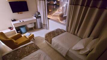 Habitación de hotel con dos camas, un escritorio, una silla, un televisor y una ventana con cortinas.