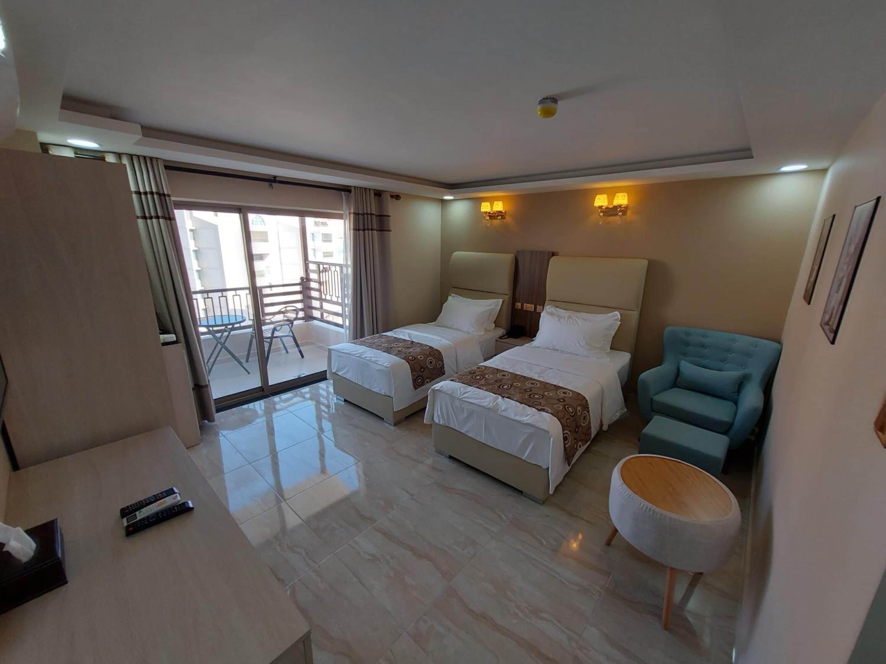 A hotel room with two beds, a balcony, a blue armchair, and a small round table.
