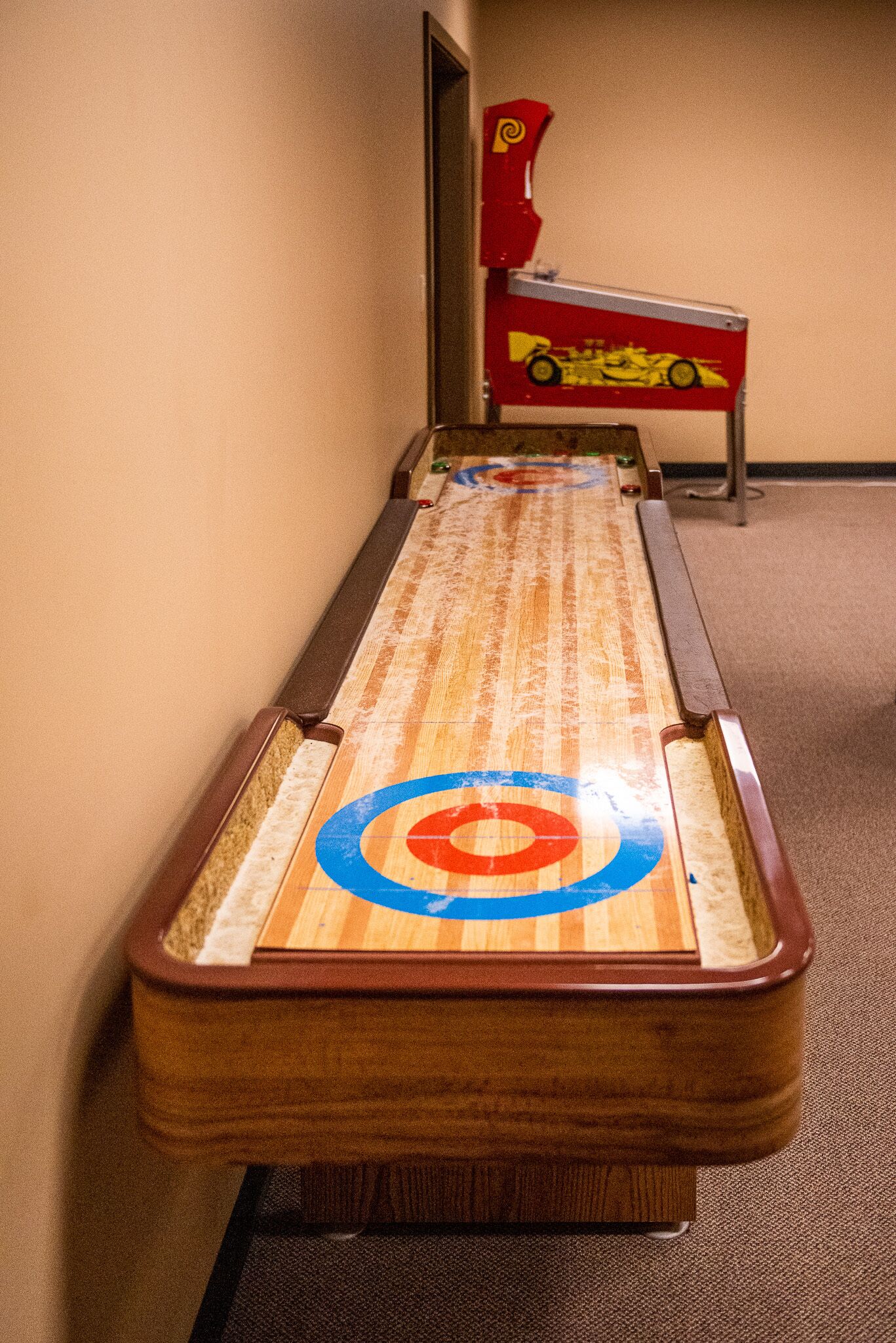 Une table de jeu de shuffleboard avec un motif cible, située dans un couloir dont le sol est recouvert de moquette.