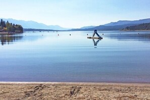 Ein ruhiger See mit einem hölzernen Steg, der sich ins Wasser erstreckt, umgeben von Bergen und einem klaren Himmel.
