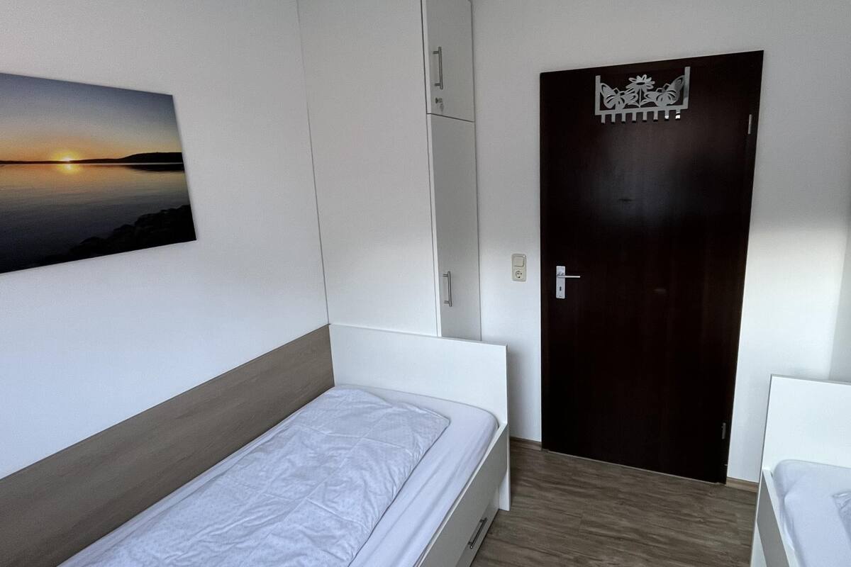 A bedroom with a bed, a wardrobe, a door with a decorative panel, and a wall-mounted picture.