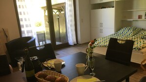 Un coin repas avec une table dressée pour deux personnes, un panier de petits pains, une bouteille de vin et un vase rempli de fleurs.