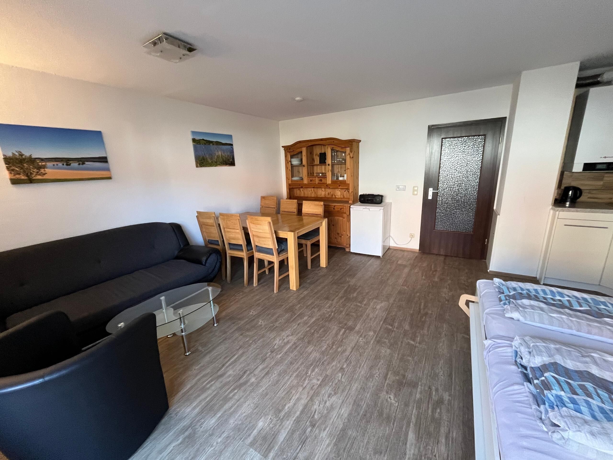 A room with a sofa, a dining table with chairs, a small kitchenette, and a door with a frosted glass panel.