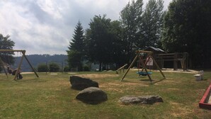 A playground with swings and a small building, surrounded by trees and a grassy area. - Ferienwohnung Hüttenzauber (Sankt Englmar)
