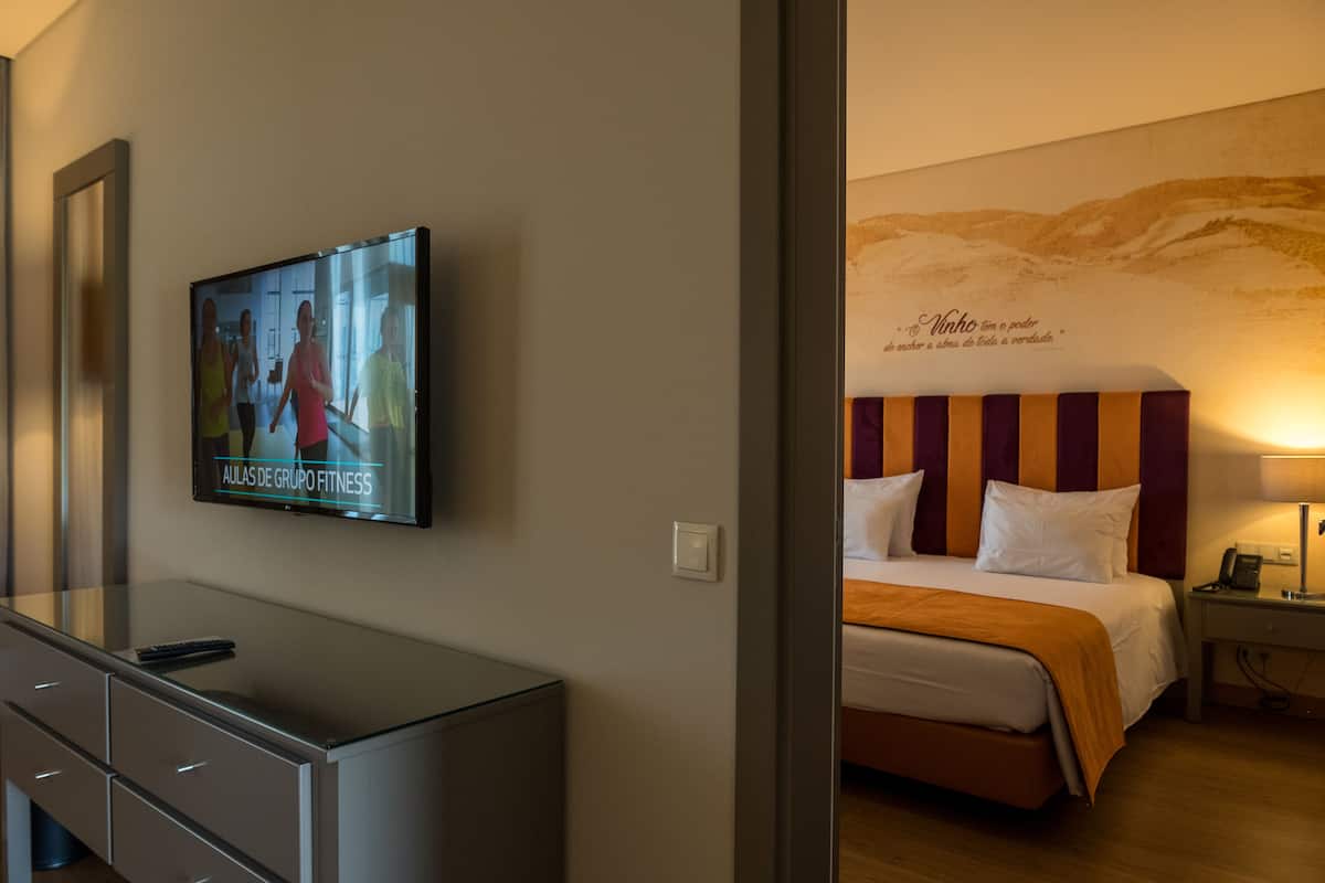 Une chambre d’hôtel comprenant un lit, un téléviseur fixé au mur, une table de chevet avec une lampe et un mur orné d’une fresque décorative.