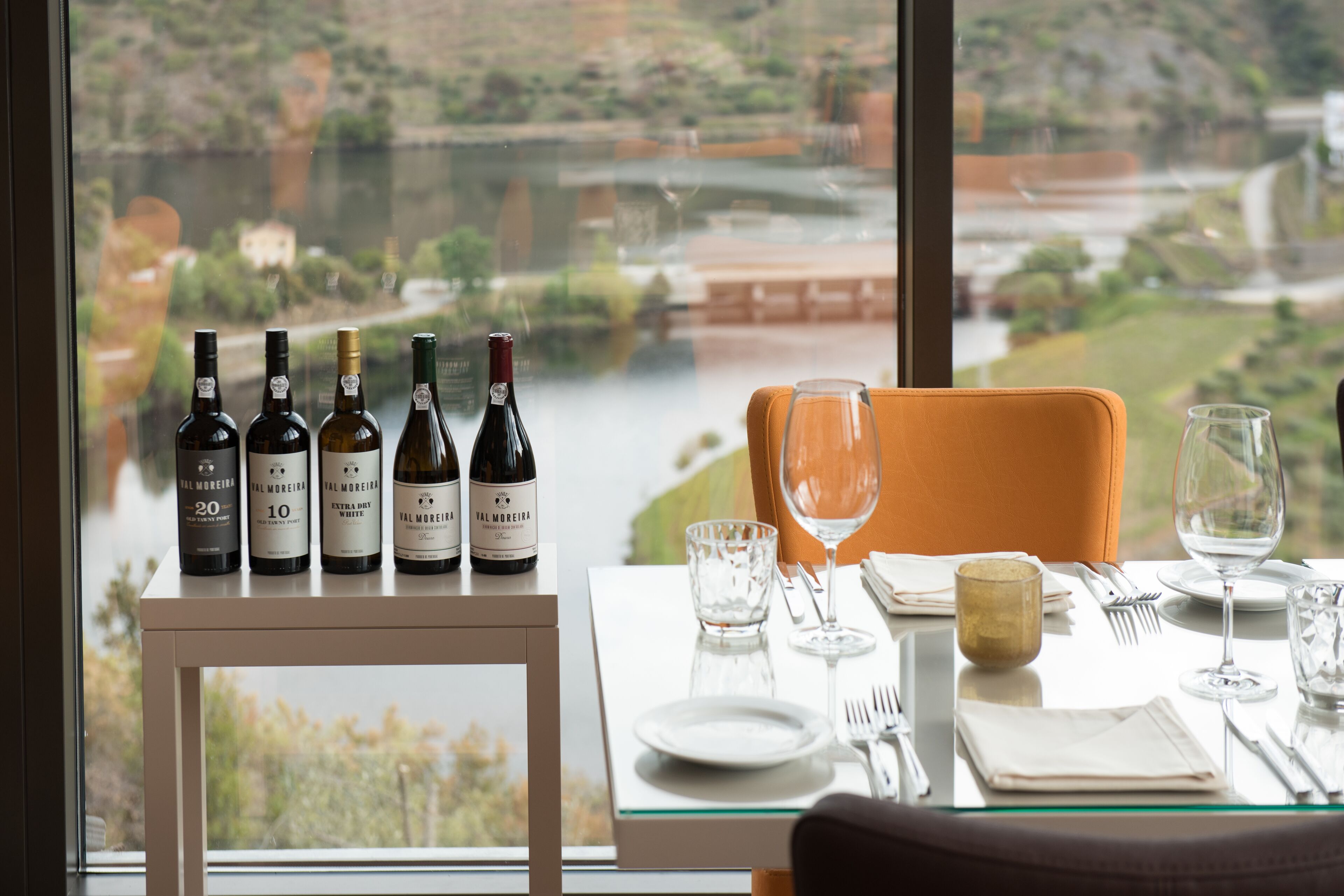 A dining table with wine bottles, glasses, and cutlery set against a scenic view.