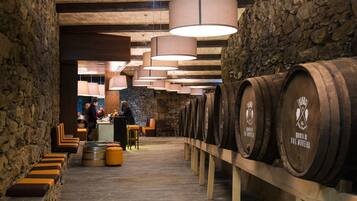 A wine cellar with wooden barrels, stone walls, and seating areas.