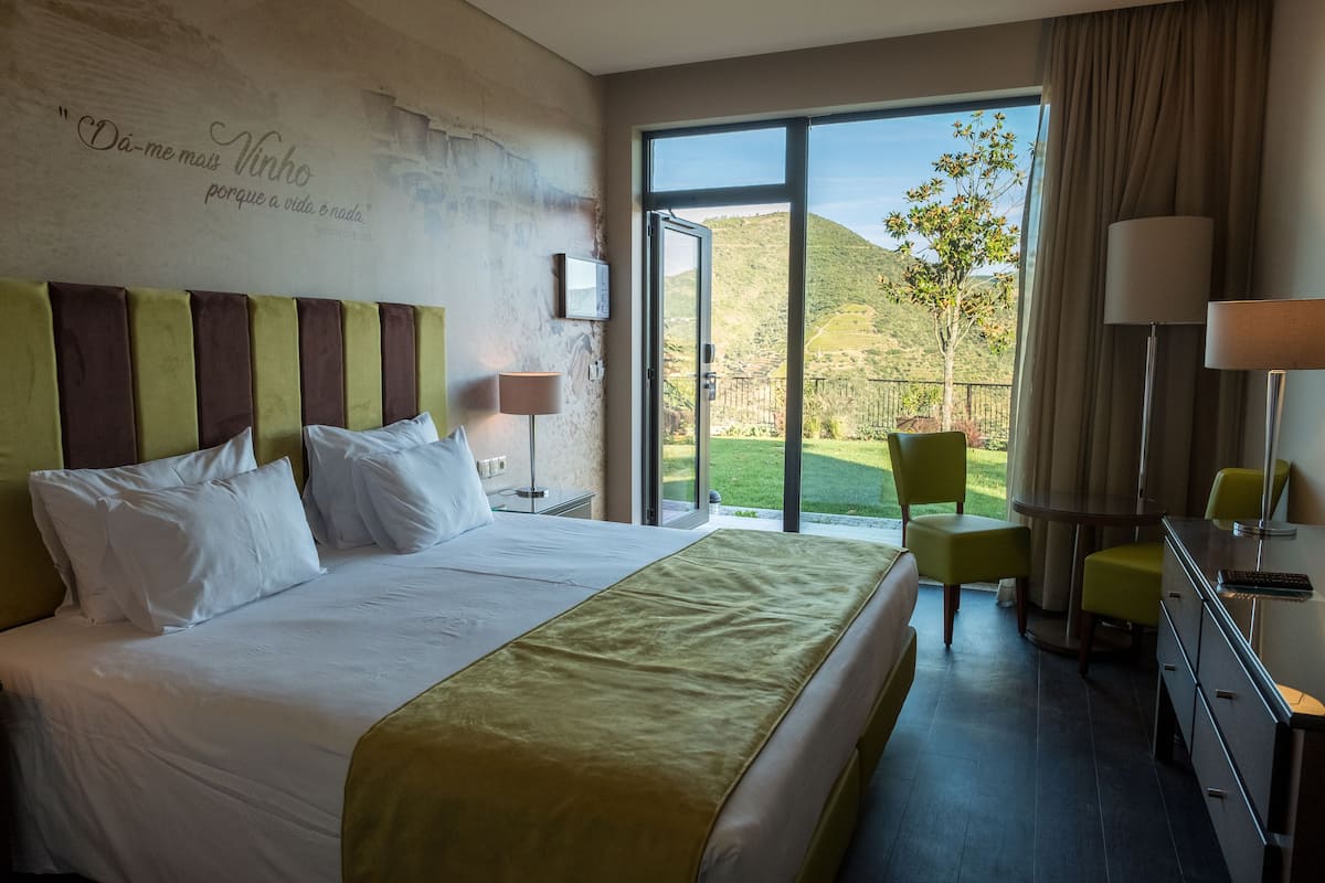 Une chambre d’hôtel avec un grand lit, une vue sur l’extérieur, un bureau avec une chaise et une lampe.