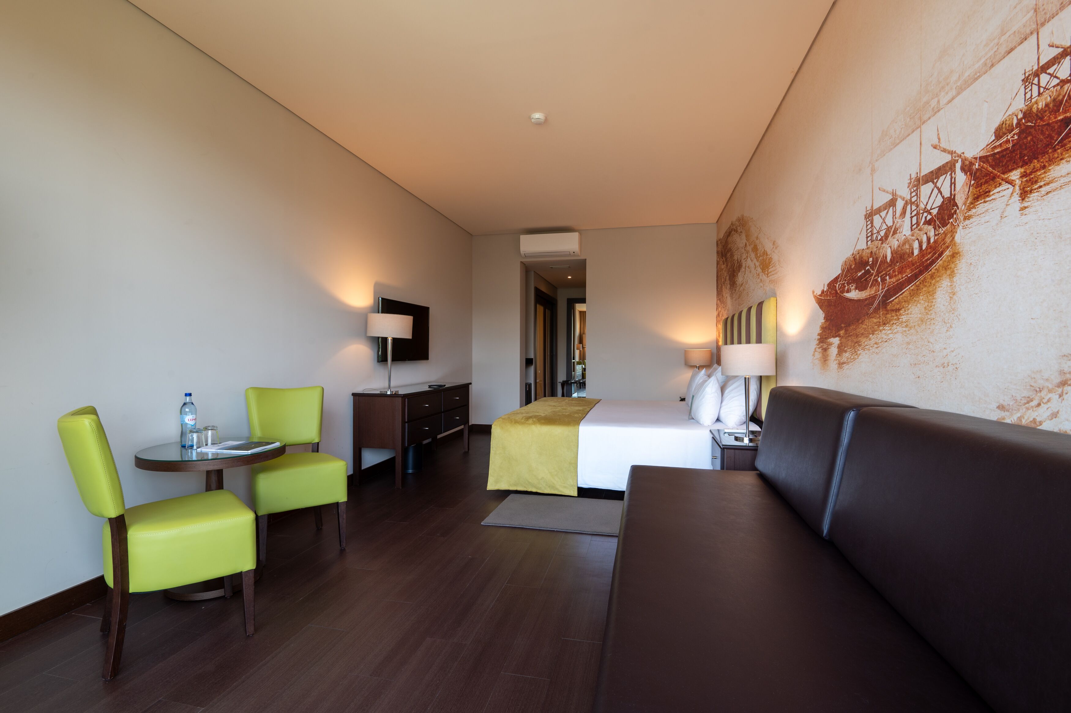 Una habitación de hotel con cama, sofá, una mesa de comedor con sillas y un mural grande en la pared.
