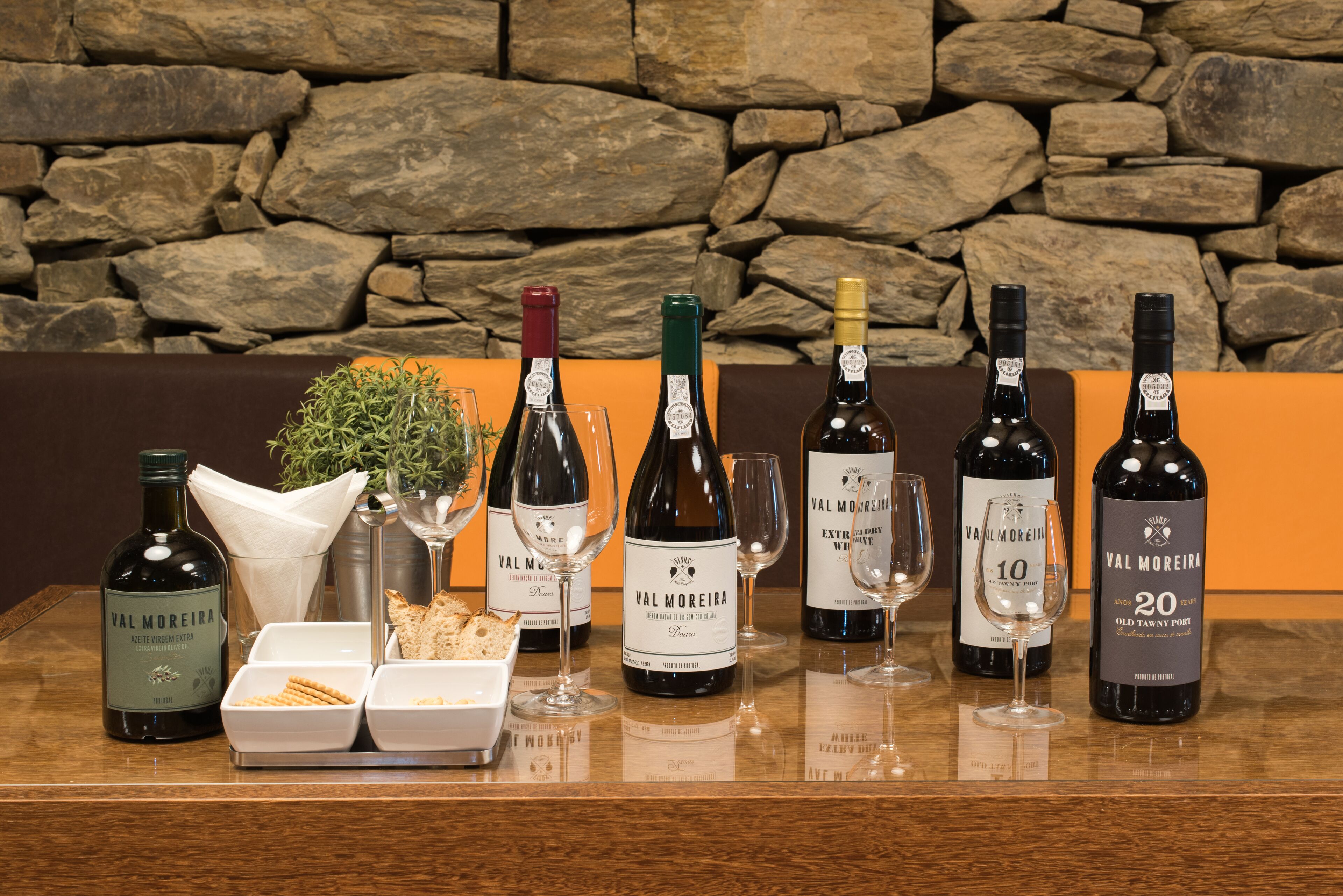 Varias botellas y copas de vino Val Moreira sobre una mesa de madera, con un fondo de pared de piedra.