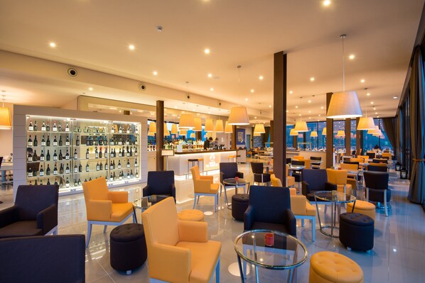 A modern hotel lobby with a bar area, seating arrangements, and a wine display.