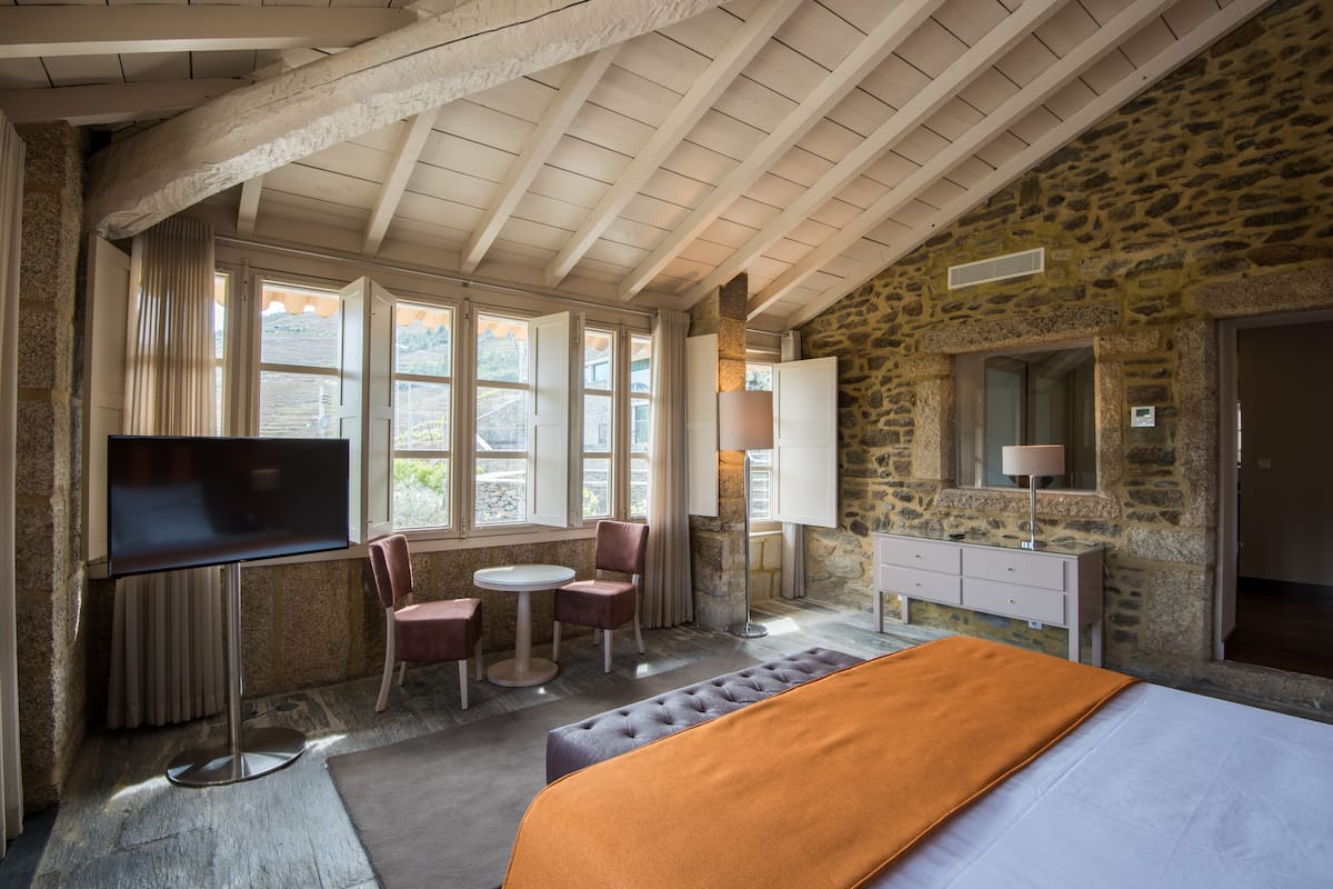 Une chambre avec un mur en pierre, un lit, une télévision, un bureau et une chaise.