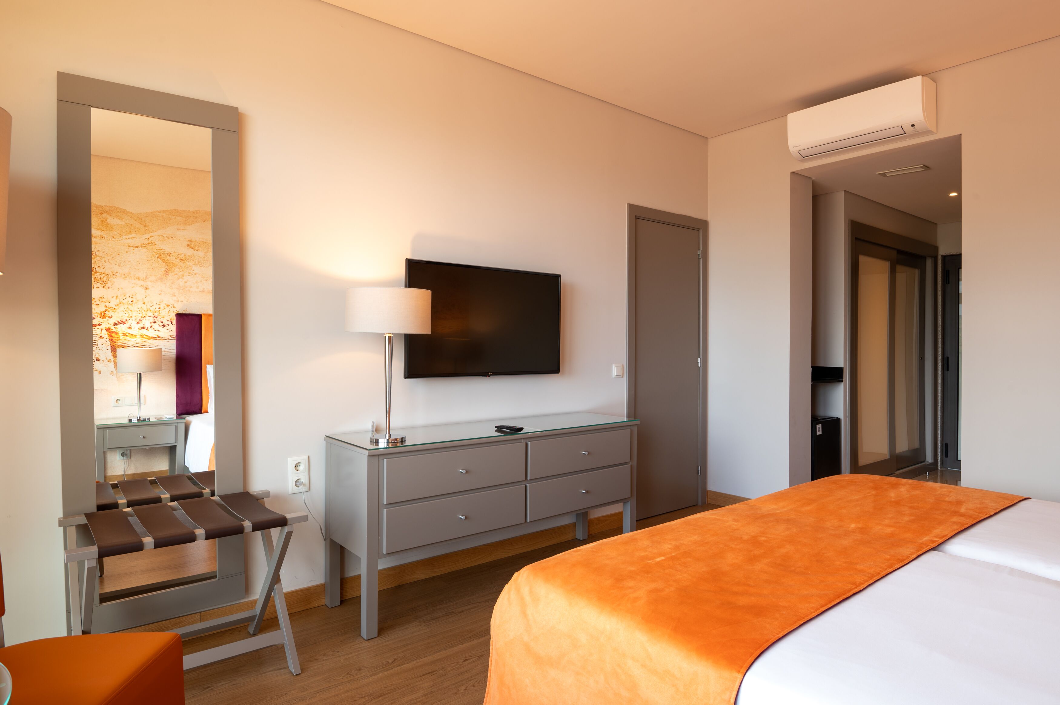 Una habitación de hotel moderna con una cama, un escritorio con lámpara, un televisor de pantalla plana y un armario.