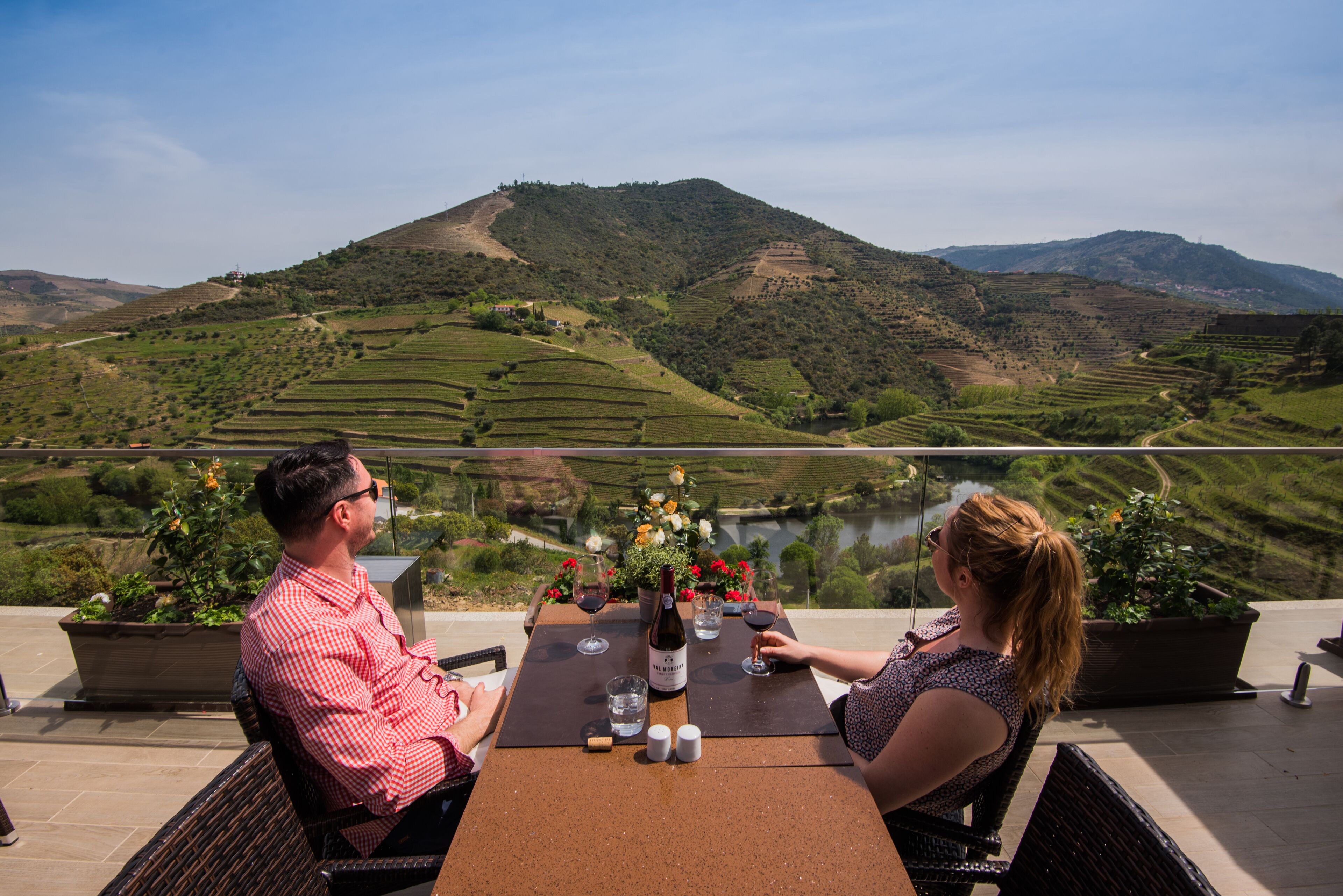 Una terraza con una mesa preparada para dos, con vistas a un paisaje montañoso y campos escalonados con un río.