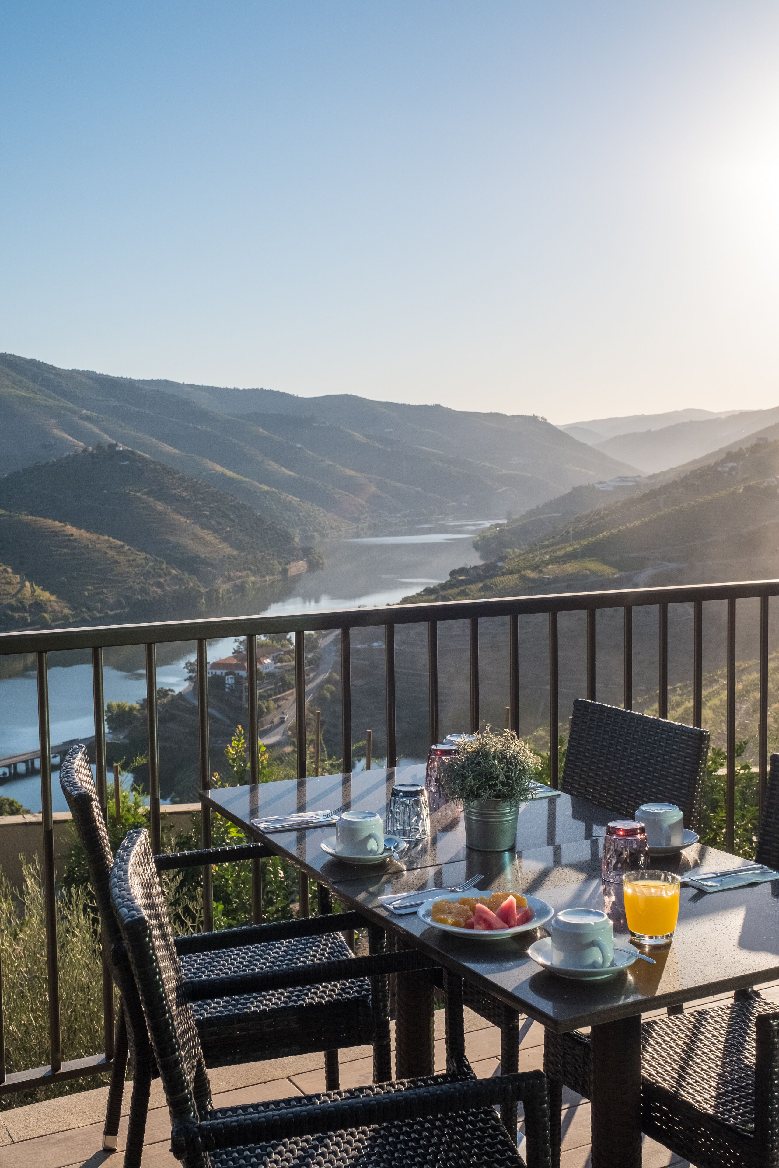 Una mesa con alimentos para el desayuno, vista a un río y colinas circundantes.