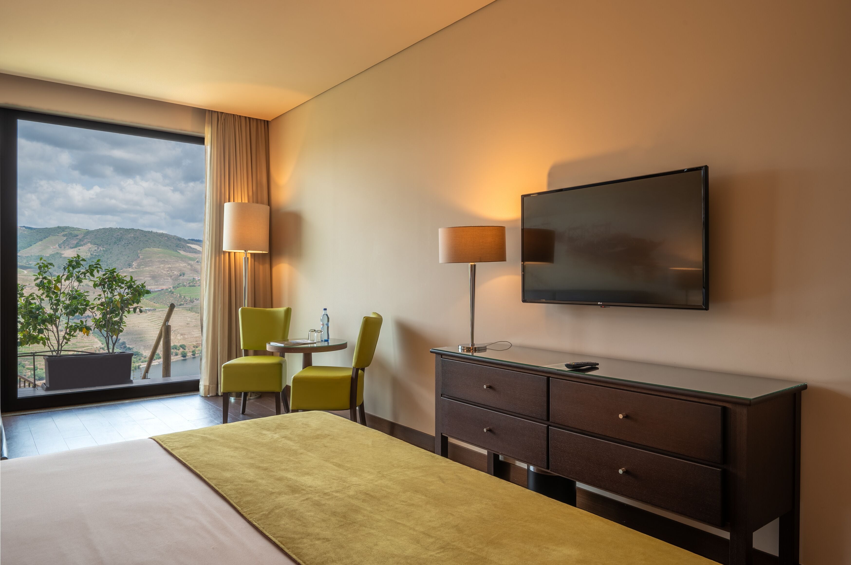 Une chambre d’hôtel comprenant un lit, un bureau, deux chaises, une télévision et une fenêtre donnant sur les montagnes.
