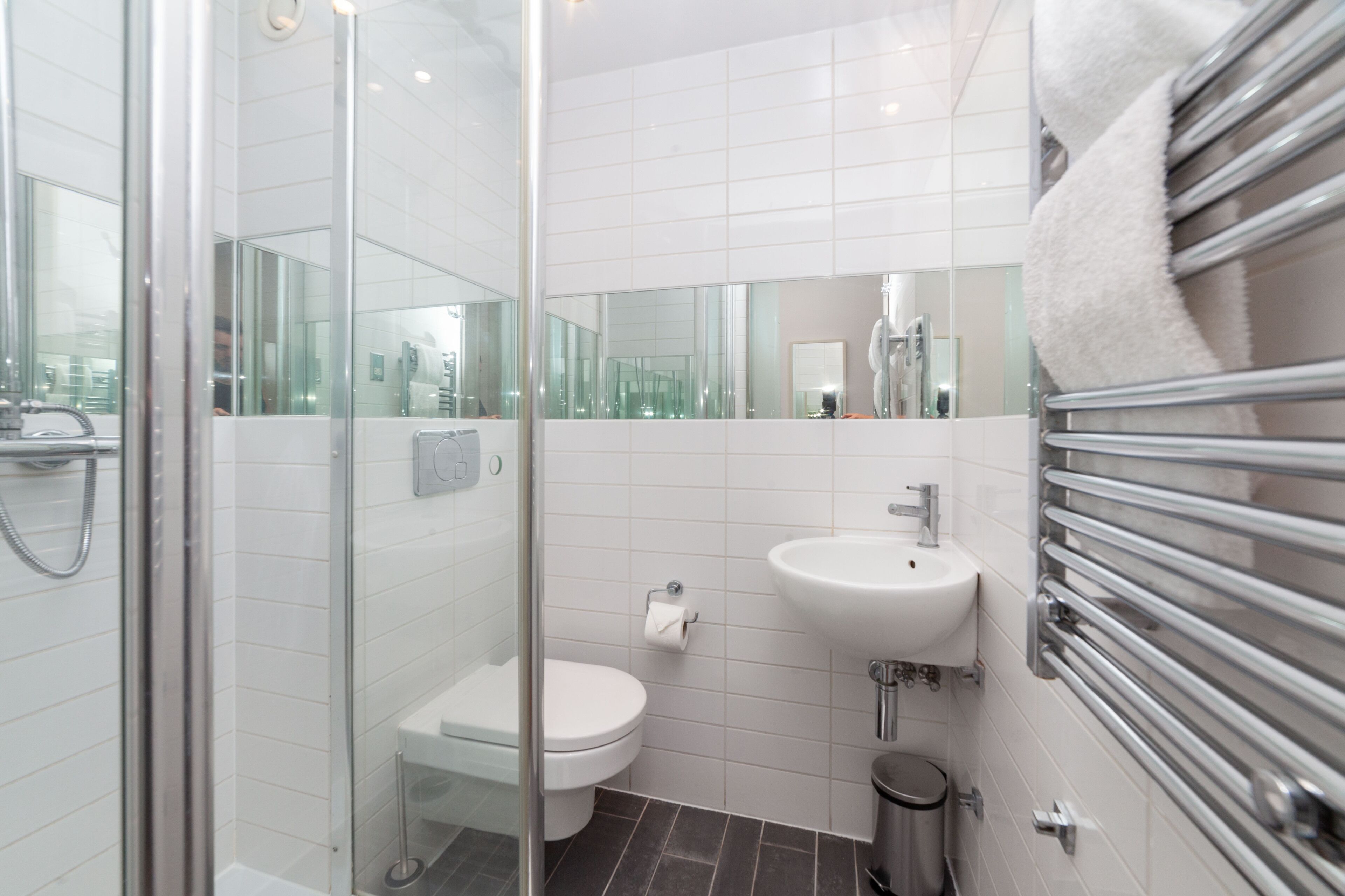 Een moderne badkamer met een douchecabine van glas, een wit toilet, een wastafel met een spiegel erboven en een handdoekrek.