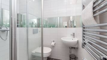 Een moderne badkamer met een douchecabine van glas, een wit toilet, een wastafel met een spiegel erboven en een handdoekrek.