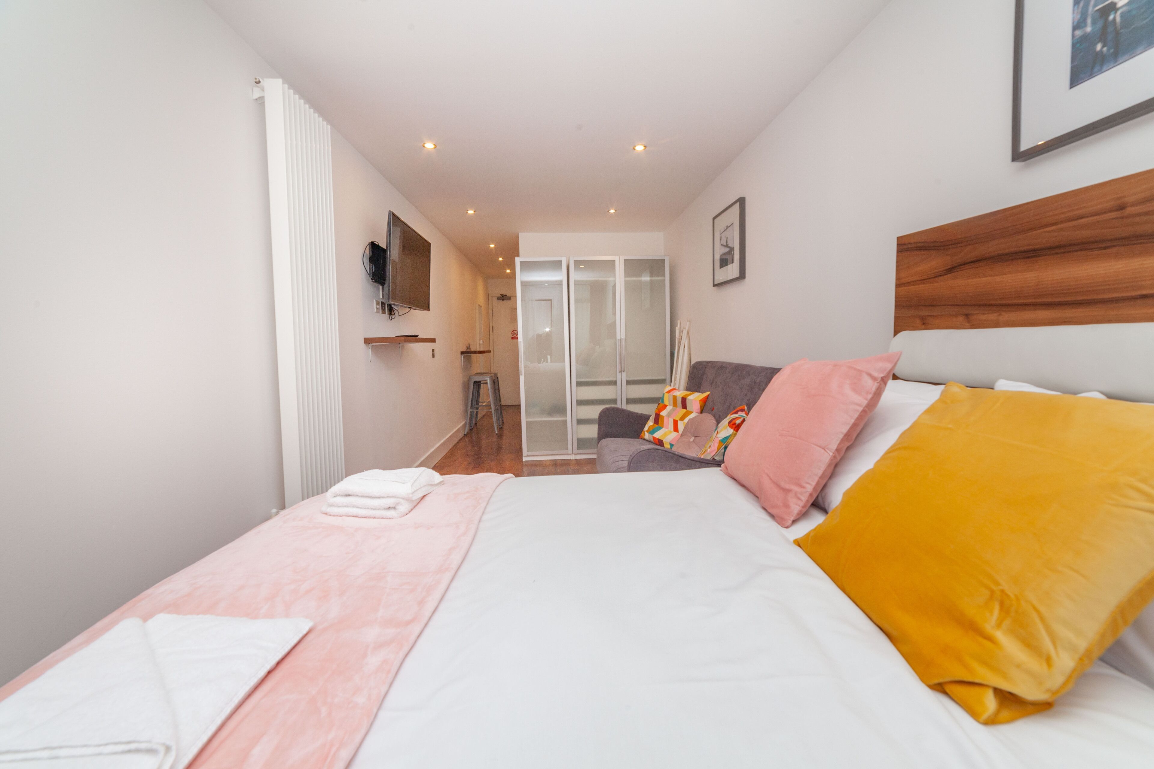 A bedroom with a bed, a bedside table, a chair, a wardrobe, and a door leading to a bathroom.