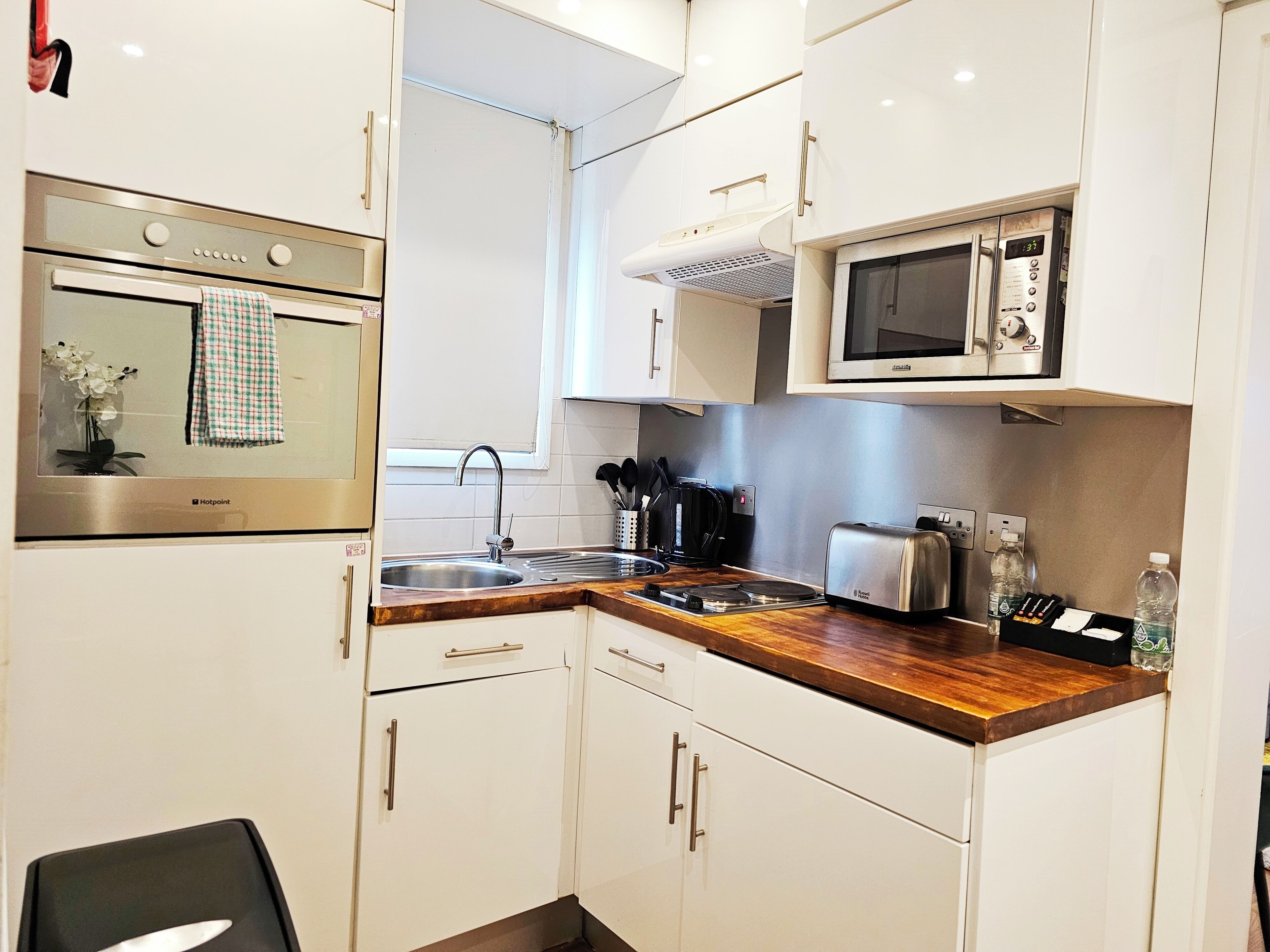 A compact kitchen with white cabinets, a stainless steel oven, a microwave, a toaster, and a sink.