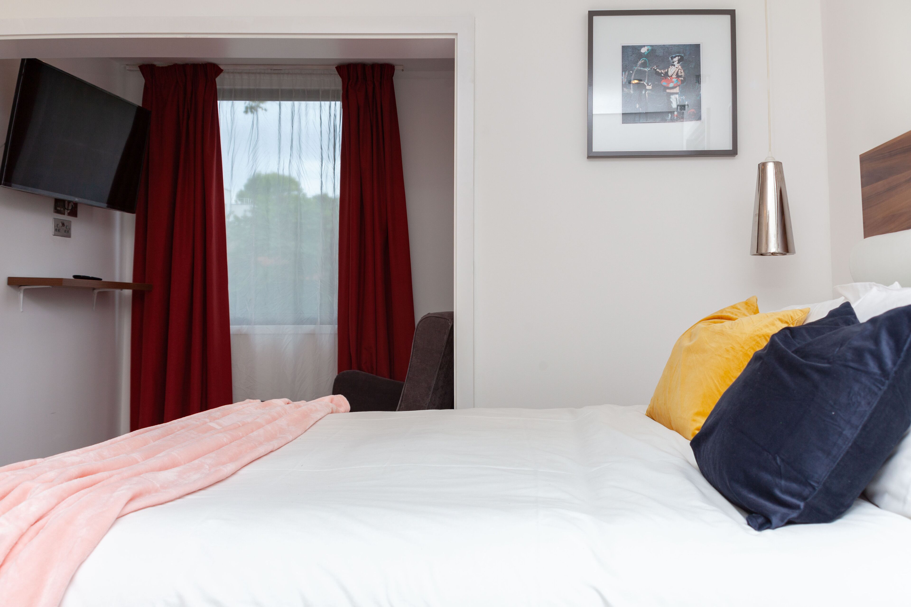 A hotel room with a bed, a TV mounted on the wall, a framed picture, and a bedside table.