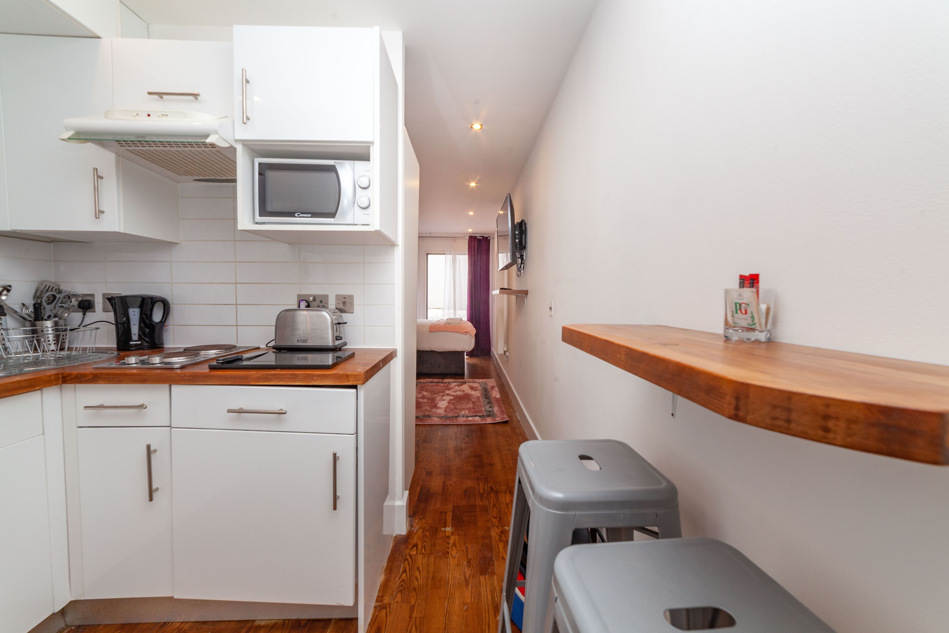 A compact kitchen with white cabinets, a microwave, a toaster, and a wooden countertop.