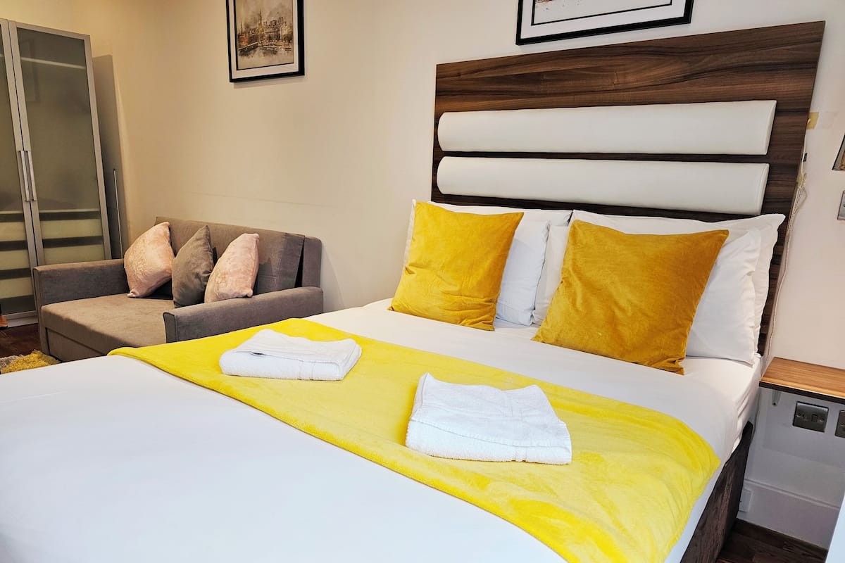 A neatly made bed with a yellow and white bedspread, two pillows, and two folded towels.