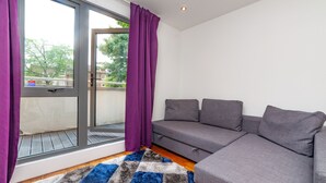 Een moderne woonkamer met een grijze bank, paarse gordijnen en een geruit tapijt.