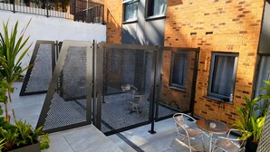 Een terras met een metalen hek, een tafel, stoelen en potplanten.