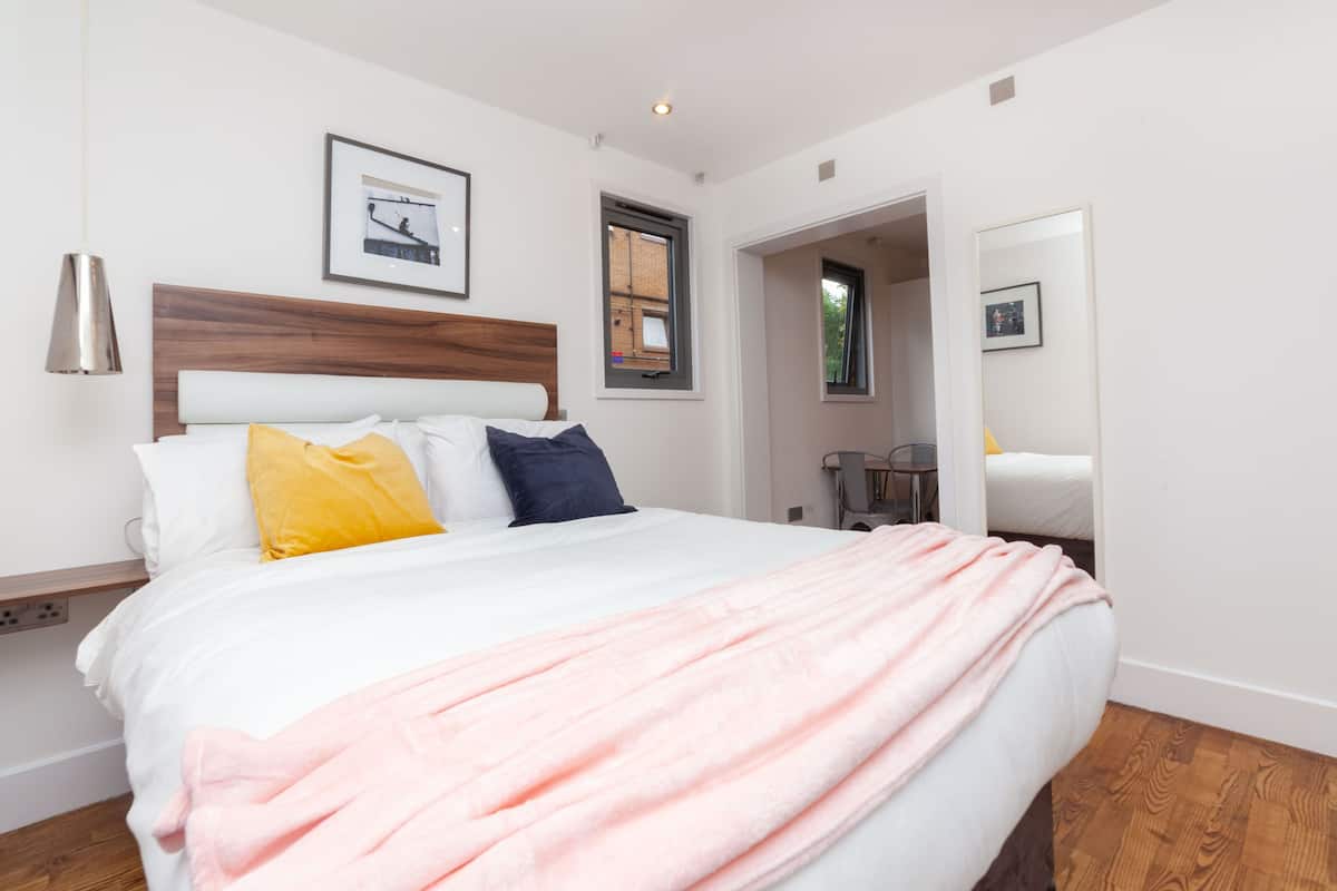 A modern bedroom with a large bed, a wooden headboard, and a pink blanket.