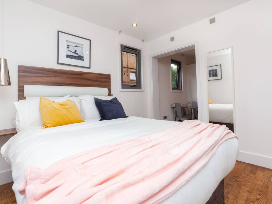 A modern bedroom with a large bed, a wooden headboard, and a pink blanket.