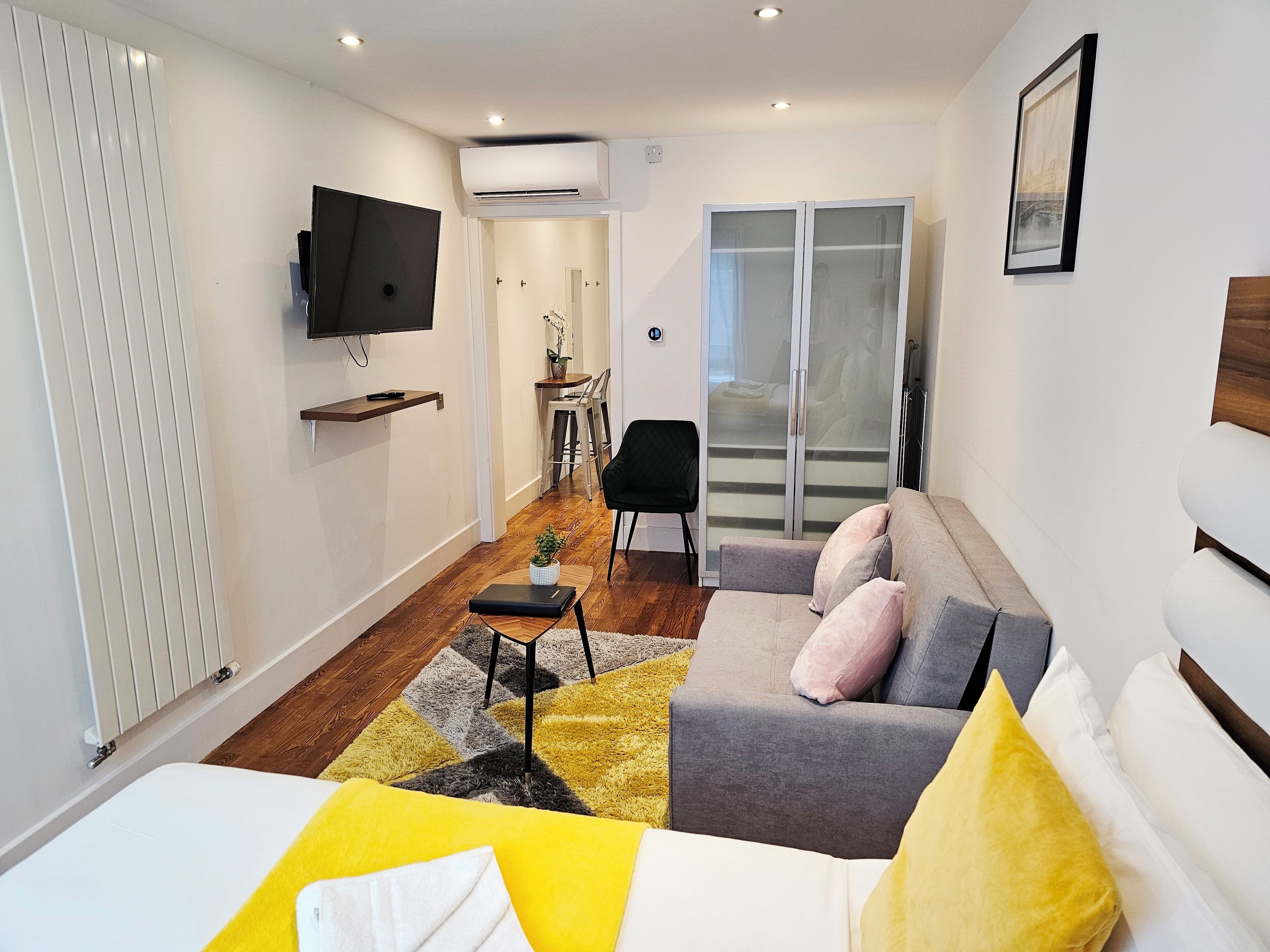 Ein modernes Hotelzimmer mit einer Couch, einem kleinen Tisch, einem Fernseher und einer Glastür, die auf einen Balkon führt.