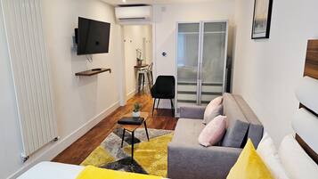 Habitación de hotel moderna con sofá, una mesita, televisor y puerta corrediza de vidrio que da a un balcón.