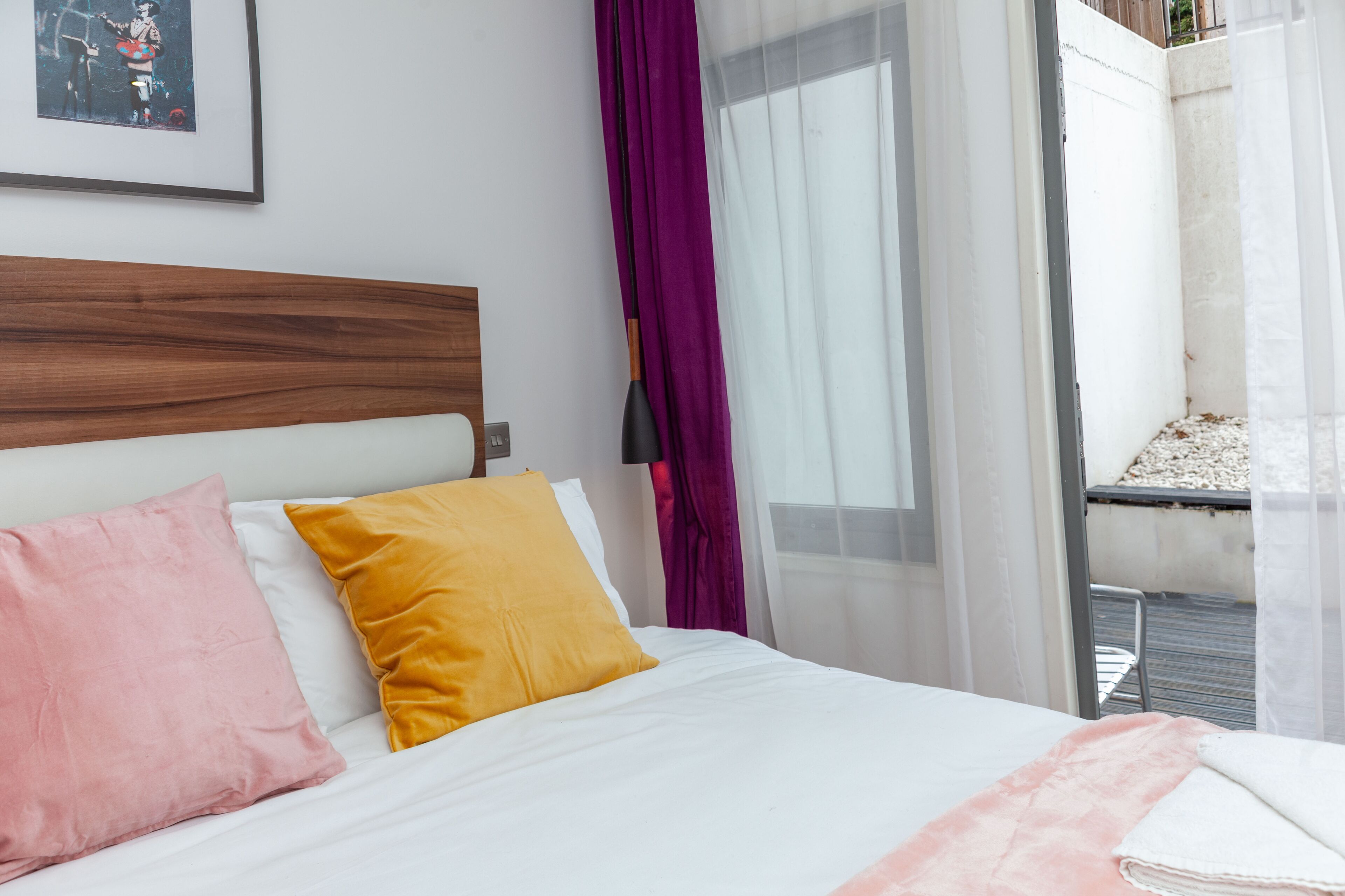 A bed with a wooden headboard, two pillows, a white bedspread, and a pink blanket.