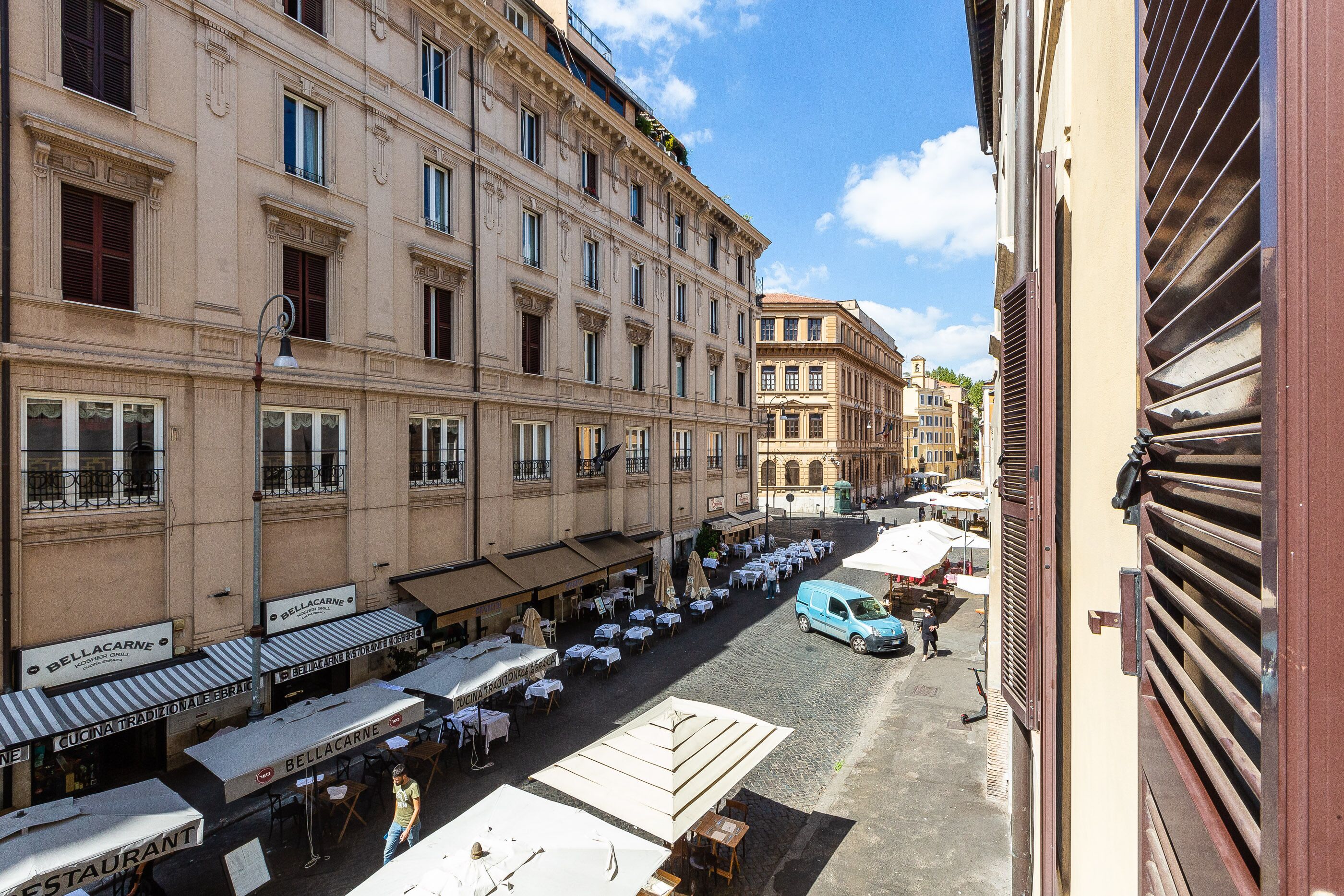 Vista da rua mostrando uma fileira de restaurantes tradicionais com mesas ao ar livre, rua de paralelepípedos e edifícios históricos.