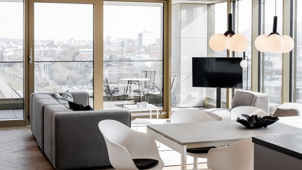 Una sala de estar moderna con un ventanal grande, un sofá, una mesa de comedor con sillas y un televisor de pantalla plana.